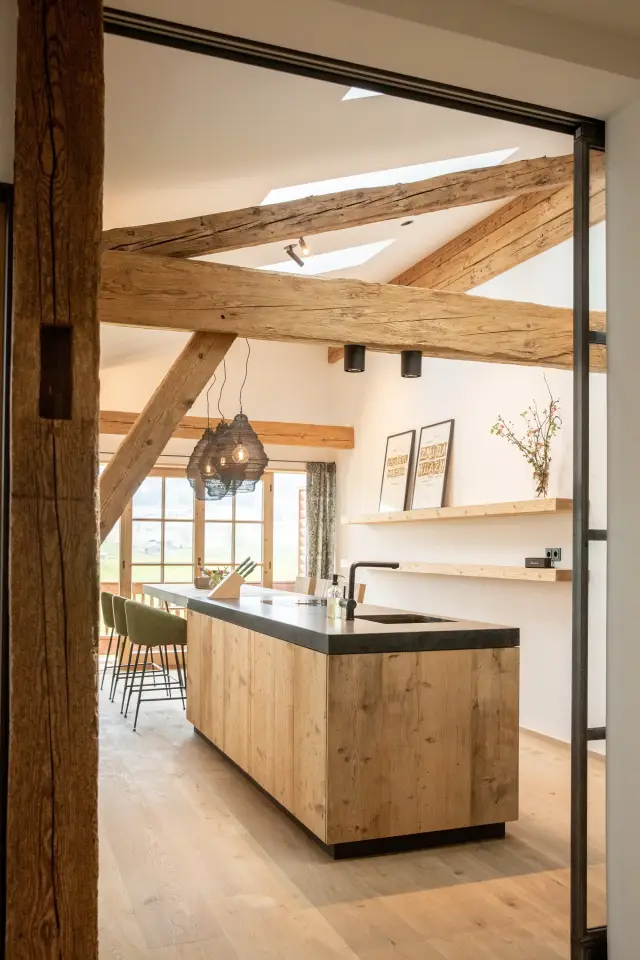 Offene Küche mit Kochinsel aus Holz im AlmSommer unter Dachbalken und Dachfenster
