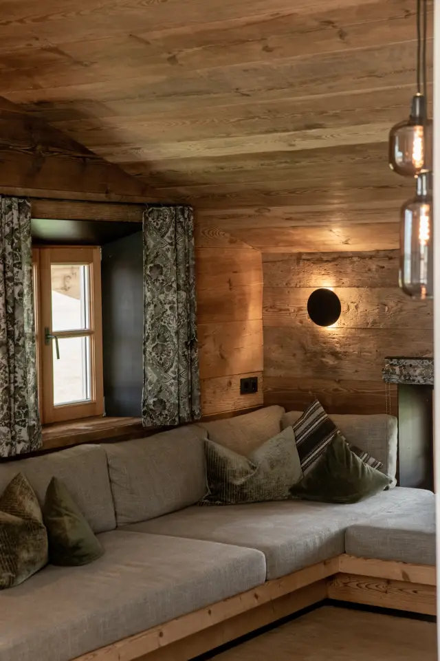 Großes Ecksofa mit Kissen im HeuLoft vor einer Holzwand mit Fenster und runder Wandleuchte