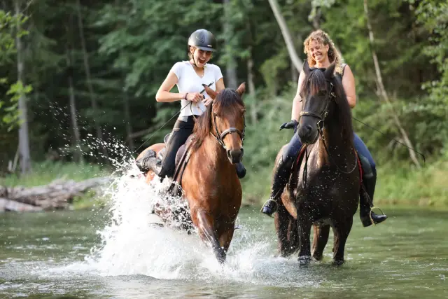 Reiter auf Ponys im flachen Wasser der Leitzach, das Wasser spritzt auf
